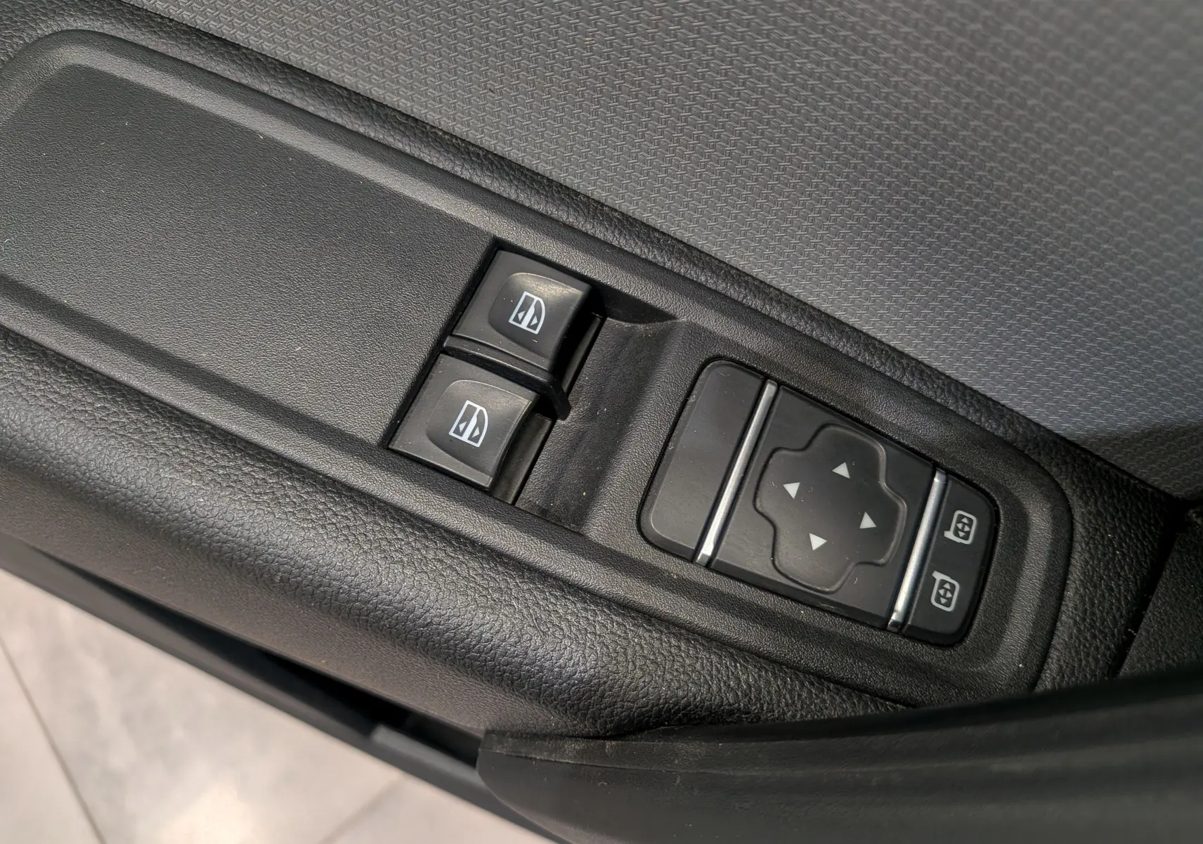 Gros plan sur les commandes de lève-vitres et réglage des rétroviseurs du côté gauche d’un Renault Kangoo blanc.