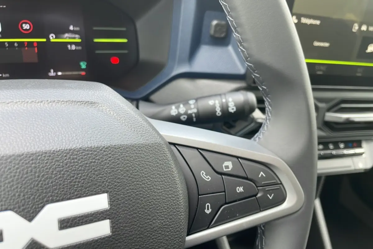 Gros plan sur le volant cuir du Dacia Bigster 2025, avec commandes multifonctions et tableau de bord numérique en arrière-plan.