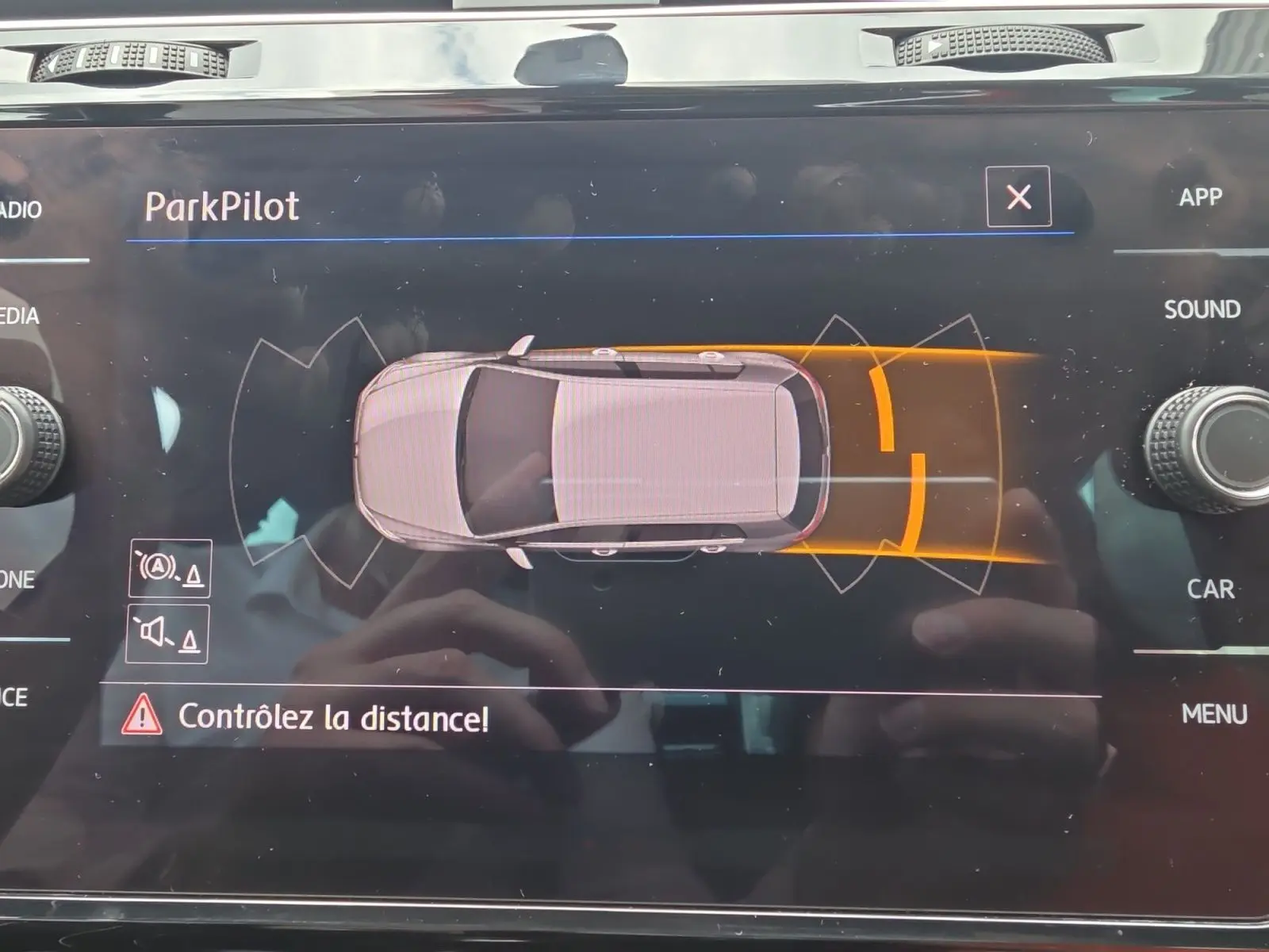 Affichage du système ParkPilot sur l'écran central d'une Volkswagen Golf noire, vue de dessus du véhicule en alerte de proximité arrière.