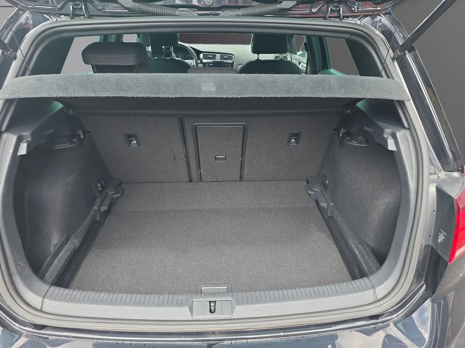 Coffre ouvert vu de l'arrière d'une Volkswagen Golf noire 1.5 TSI EVO 150 R-line, intérieur spacieux et tapis gris.