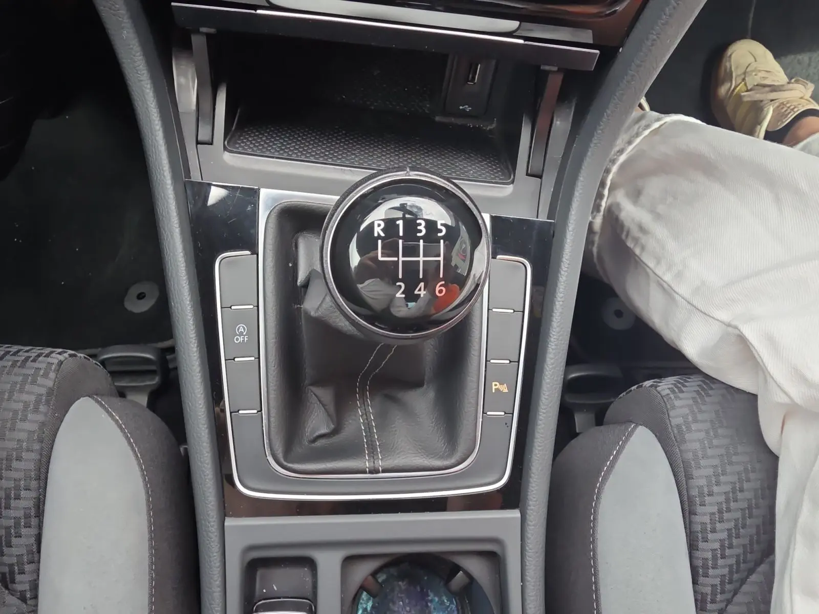 Vue rapprochée du levier de vitesses manuel noir de la Volkswagen Golf 1.5 TSI EVO 150 R-line, avec console centrale et sièges partiellement visibles.