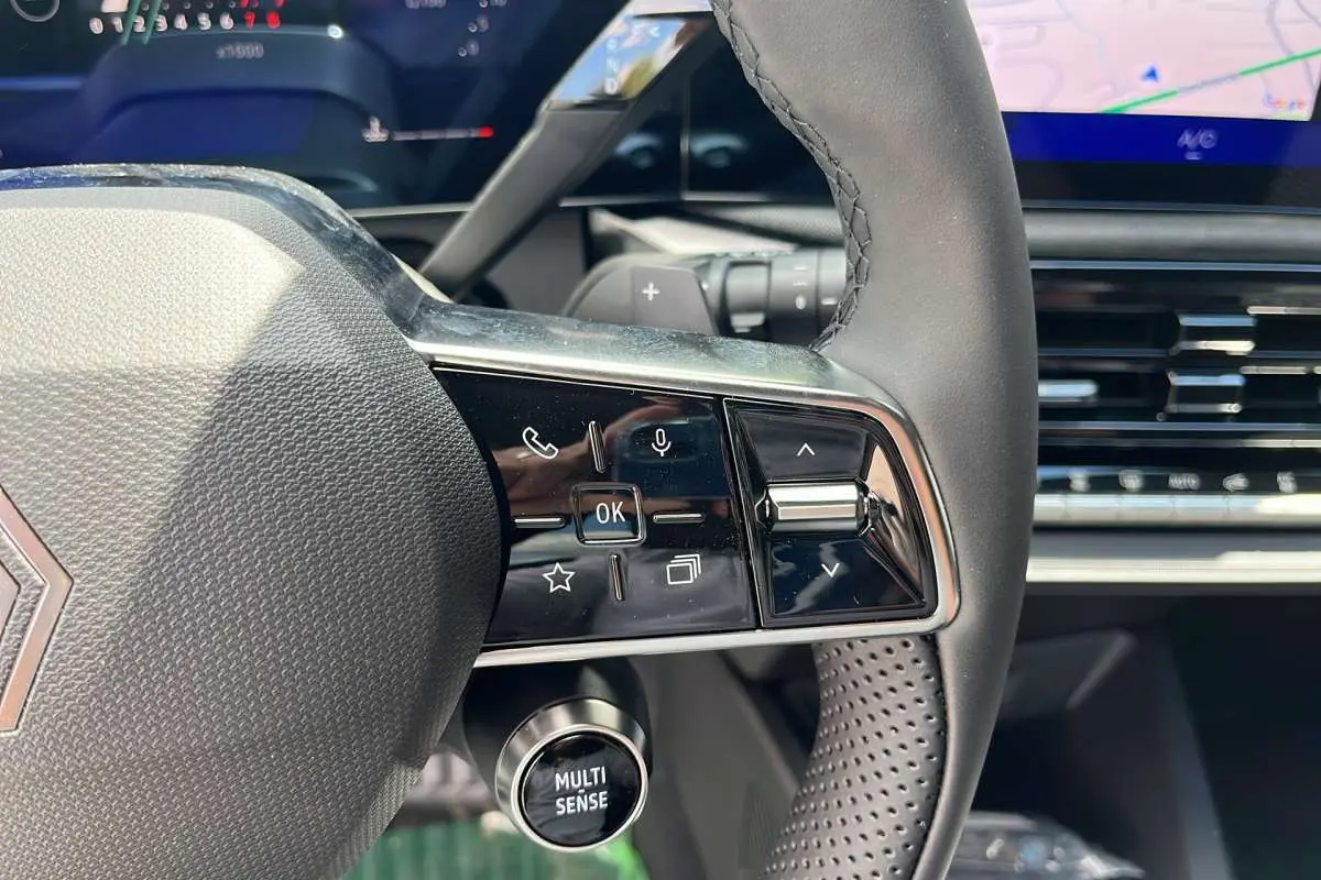 Gros plan sur le volant multifonctions textile de la Renault Clio gris schiste avec commandes intégrées et bouton Multi Sense.