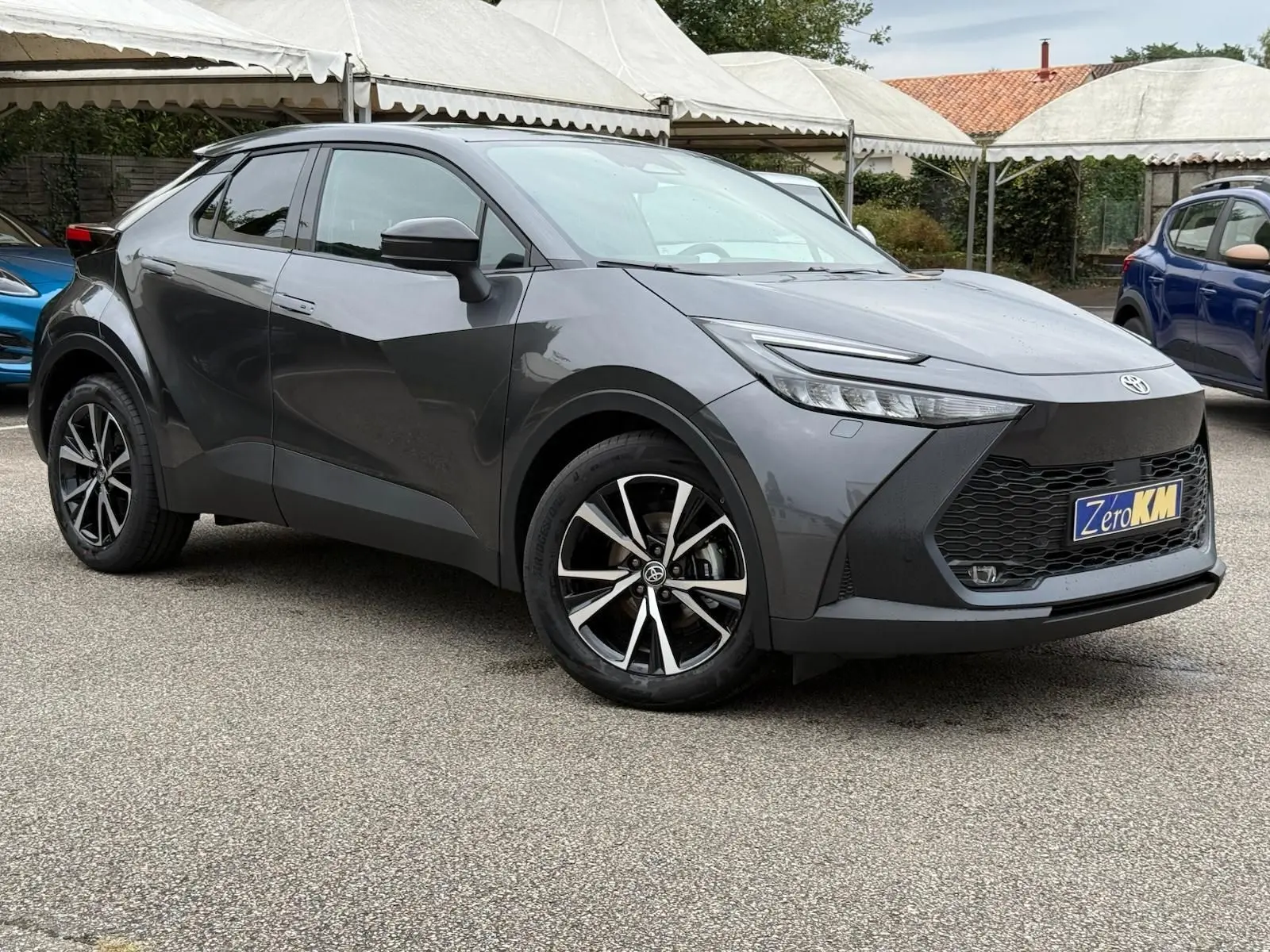 Toyota C-HR 1.8 140CH STYLE gris atlas en 3/4 avant droit, avec jantes alliage et calandre noire distinctive.