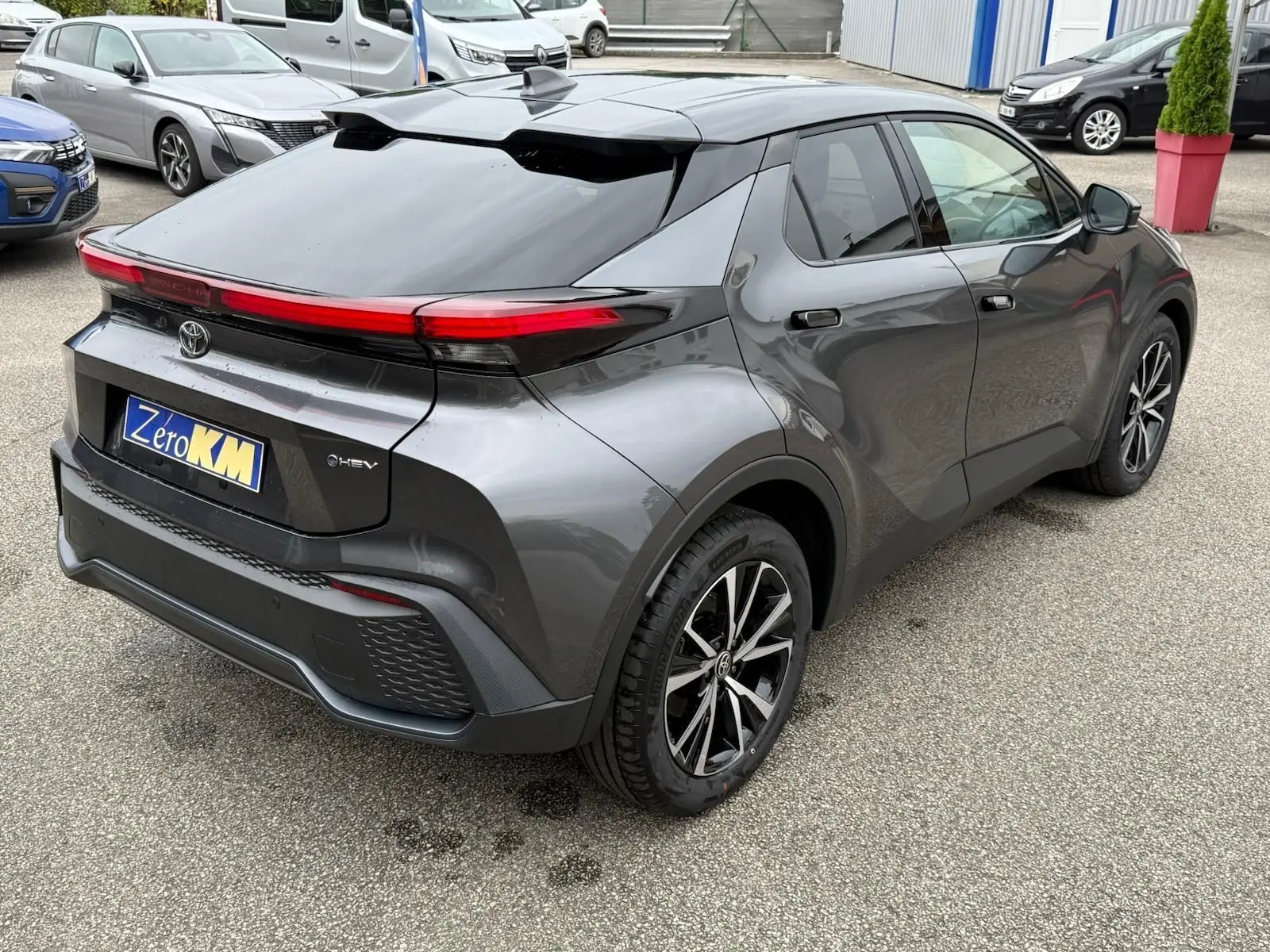 Vue 3/4 arrière droite d’un Toyota C-HR gris atlas 2025 avec feux arrière LED et jantes alliage noires et argentées.
