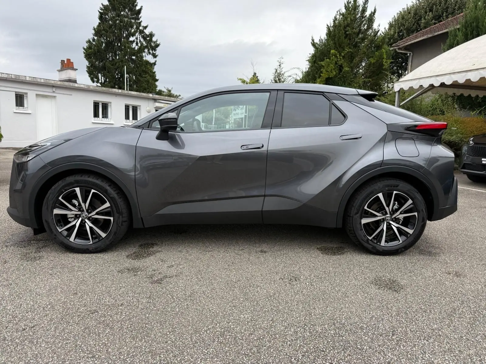 Profil côté gauche du Toyota C-HR 1.8 140CH STYLE 2025 en gris atlas avec jantes alliage noires et argentées.