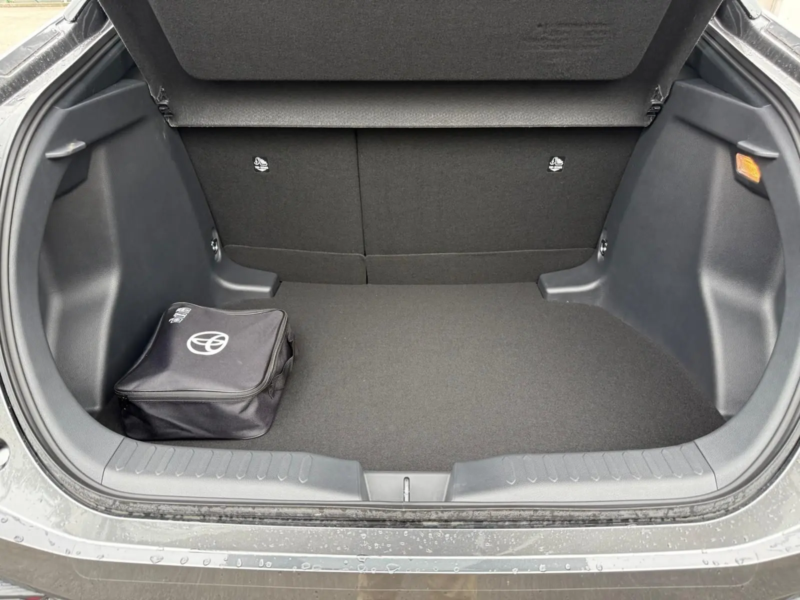 Coffre ouvert d’un Toyota C-HR gris atlas 2025, montrant un espace de chargement propre avec sac Toyota noir.