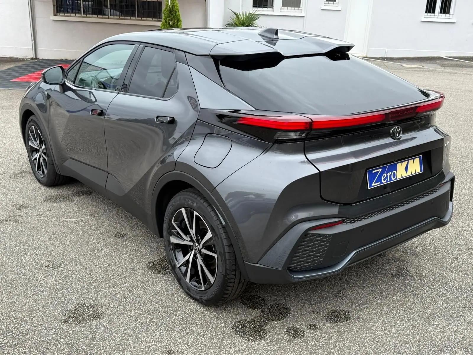 Toyota C-HR 1.8 140CH STYLE 2025 gris atlas vu en 3/4 arrière droit avec feux arrière LED continus et jantes alliage.