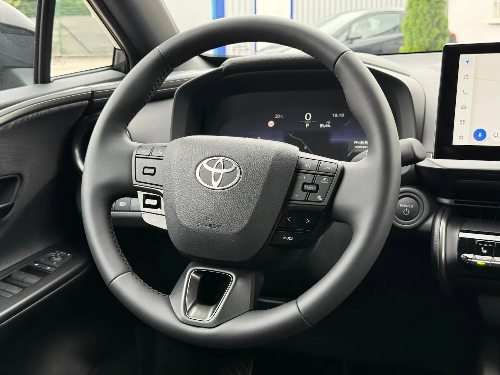 Vue rapprochée du volant multifonction noir du Toyota C-HR 1.8 140CH STYLE MY25 avec tableau de bord digital.