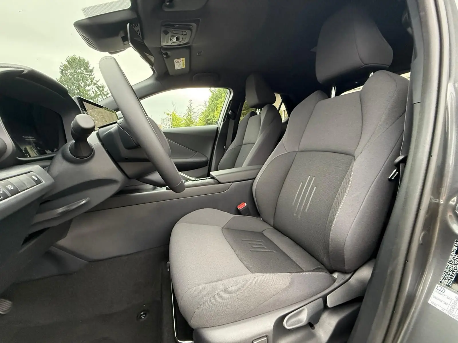 Intérieur du Toyota C-HR 1.8 140CH STYLE 2025, vue côté conducteur sur sièges tissu gris et tableau de bord moderne.
