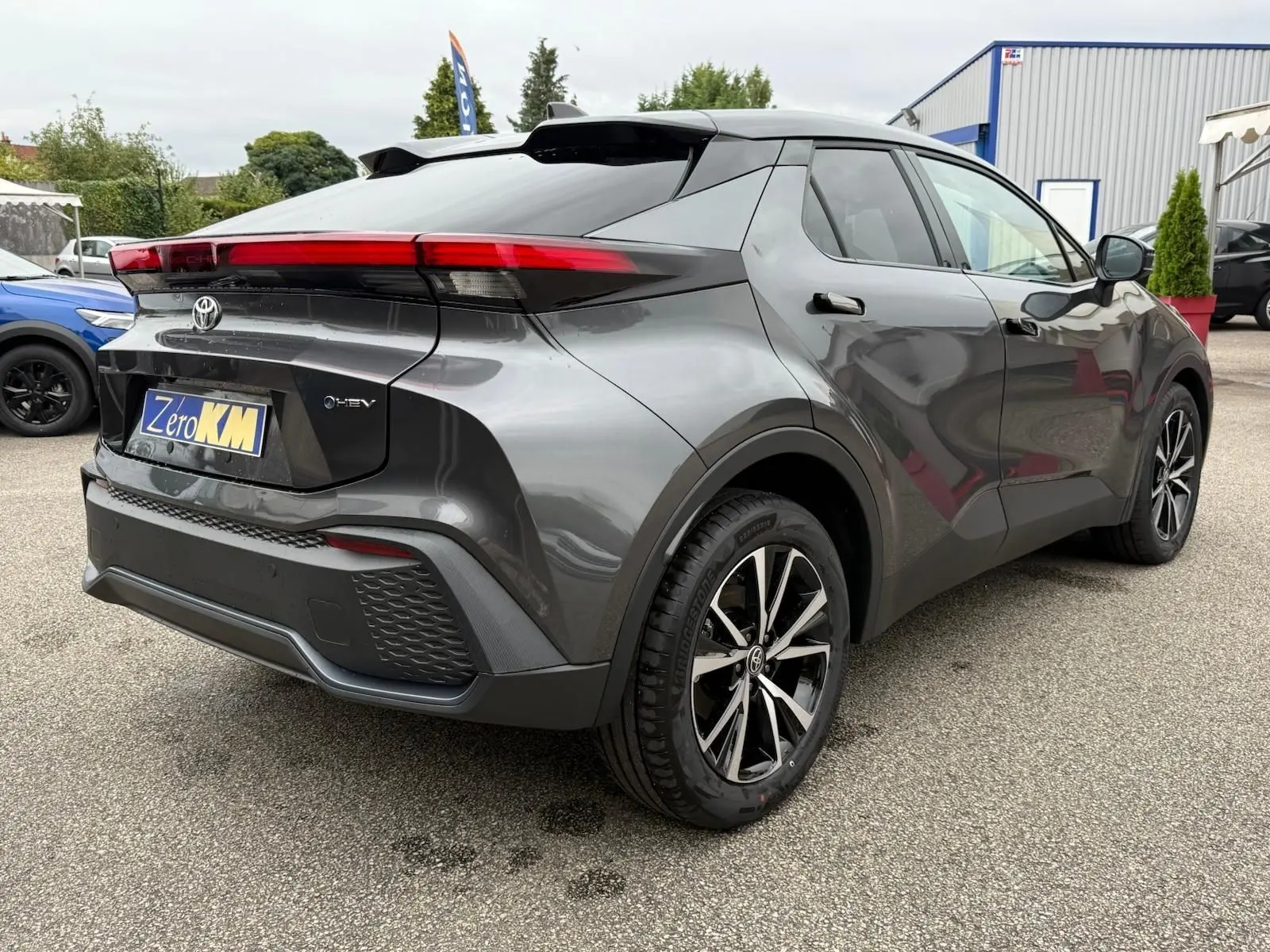 Vue 3/4 arrière droite du Toyota C-HR 1.8 140CH STYLE gris atlas avec feux arrière étirés et jantes noires bicolores.