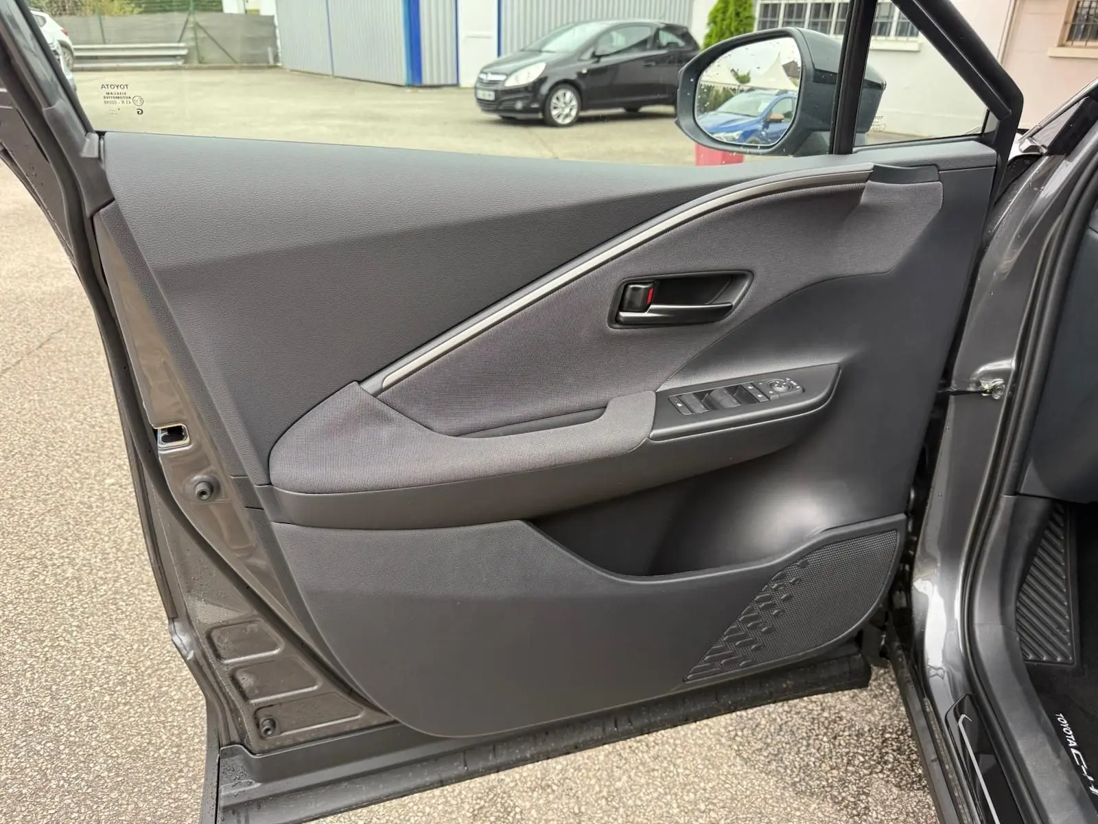 Porte avant gauche ouverte d’un Toyota C-HR gris atlas 2025, montrant les commandes de vitres et la garniture intérieure.