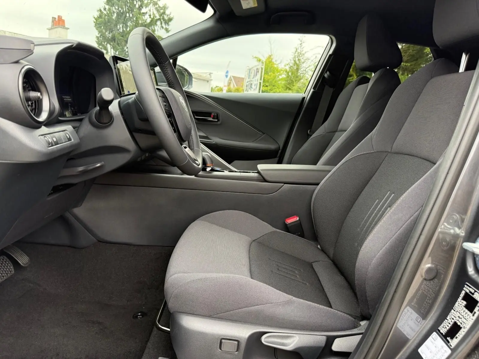 Intérieur avant droit du Toyota C-HR 1.8 140CH STYLE 2025 en gris atlas, sièges tissu gris foncé et tableau de bord moderne.