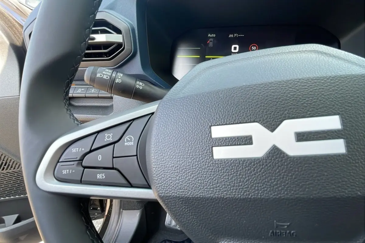 Gros plan sur le volant cuir du Dacia Bigster TCE 130 4x4, avec commandes intégrées et tableau de bord digital visible.
