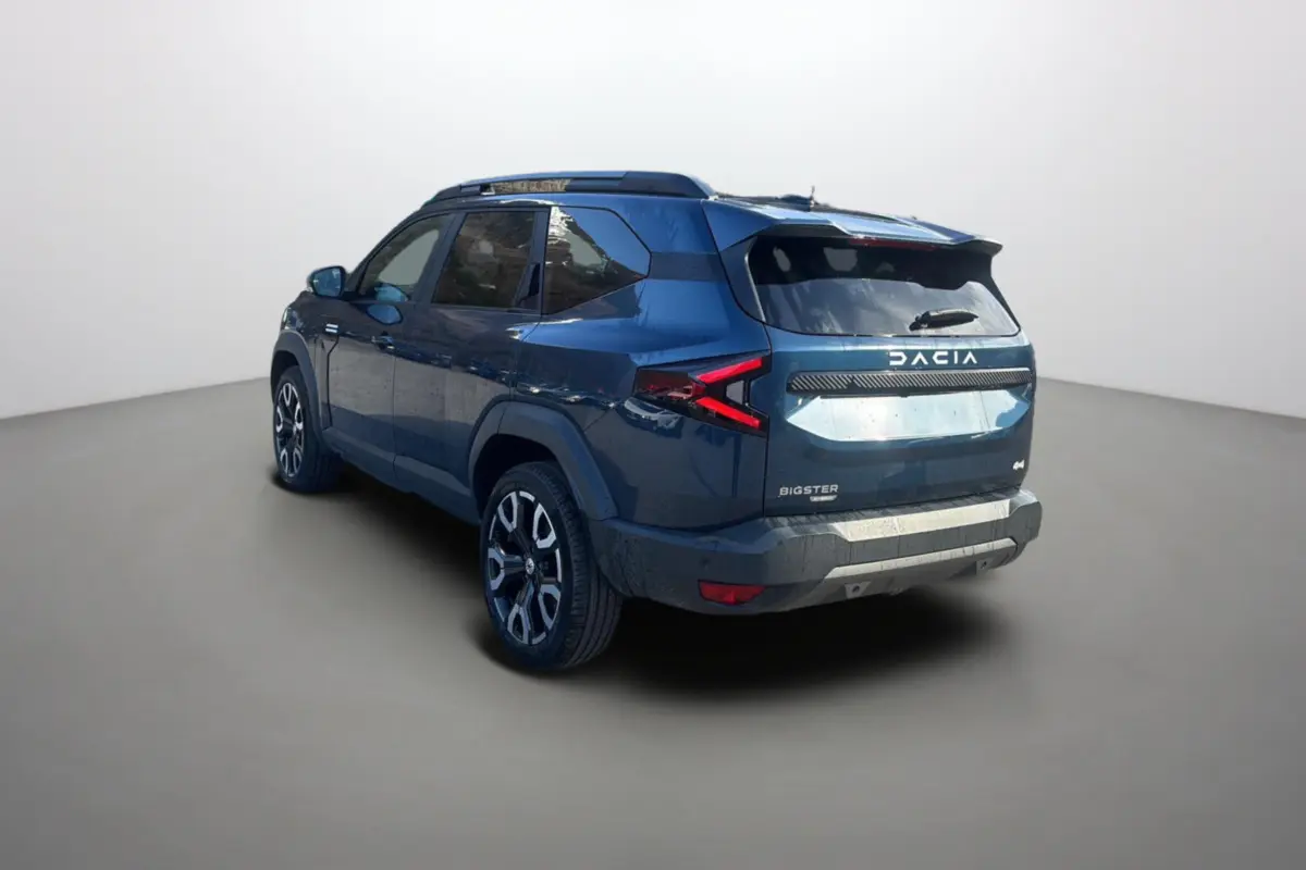 Vue 3/4 arrière droite du Dacia Bigster bleu indigo avec jantes alu 19 pouces et hayon électrique dans un studio.