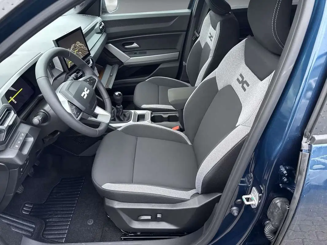 Vue intérieure côté conducteur de la Dacia Bigster bleu indigo, sièges bi-matière avec logo et tableau de bord digital.