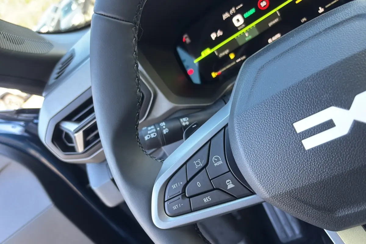 Gros plan sur le volant cuir noir de la Dacia Bigster bleu indigo, avec commandes intégrées et tableau de bord digital visible.