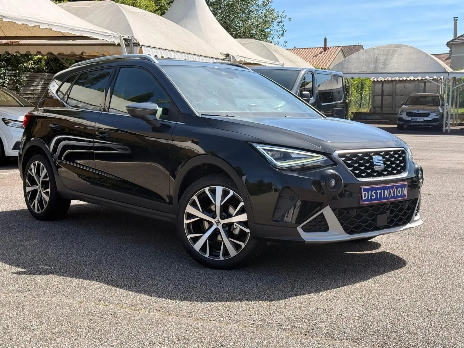 SEAT Arona noir vue 3/4 avant droit, avec jantes alliage et calandre distinctive sous un ciel ensoleillé.
