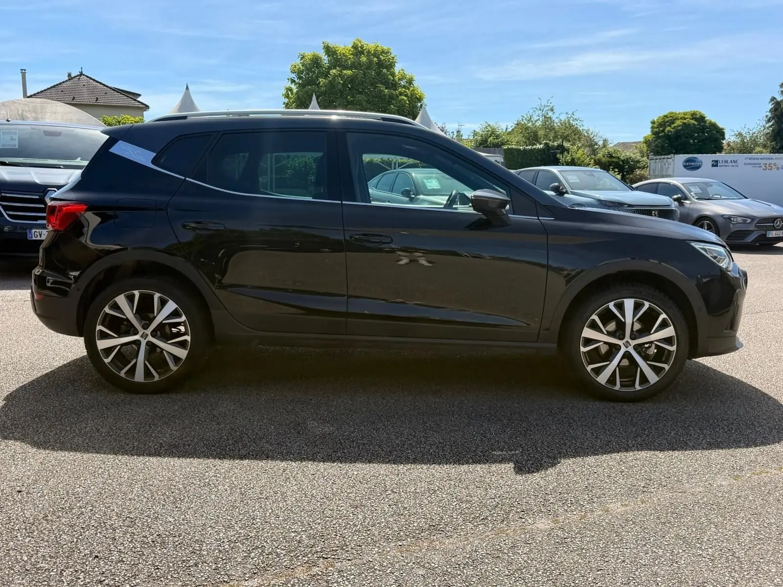Vue latérale droite d'un SEAT Arona noir 5 portes, avec jantes alliage et toit noir contrasté sous un ciel bleu.