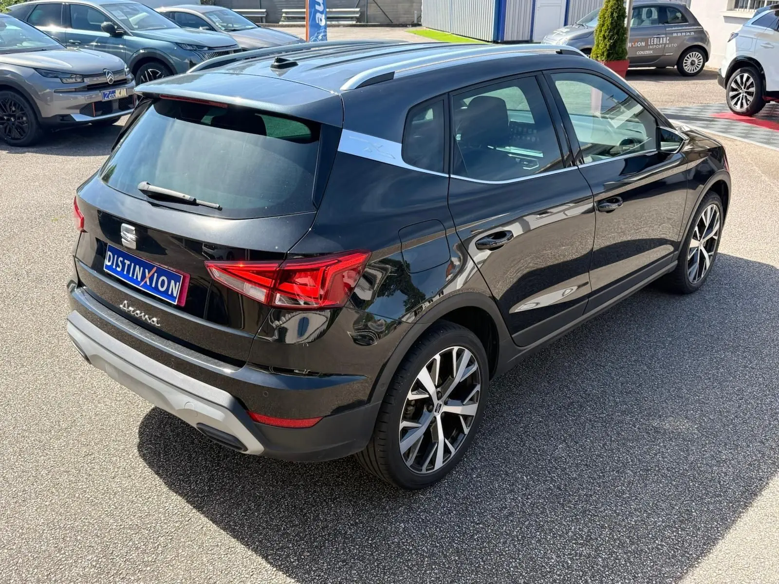 Vue 3/4 arrière droite d'un SEAT Arona noir avec jantes alliage et barres de toit chromées sur parking.