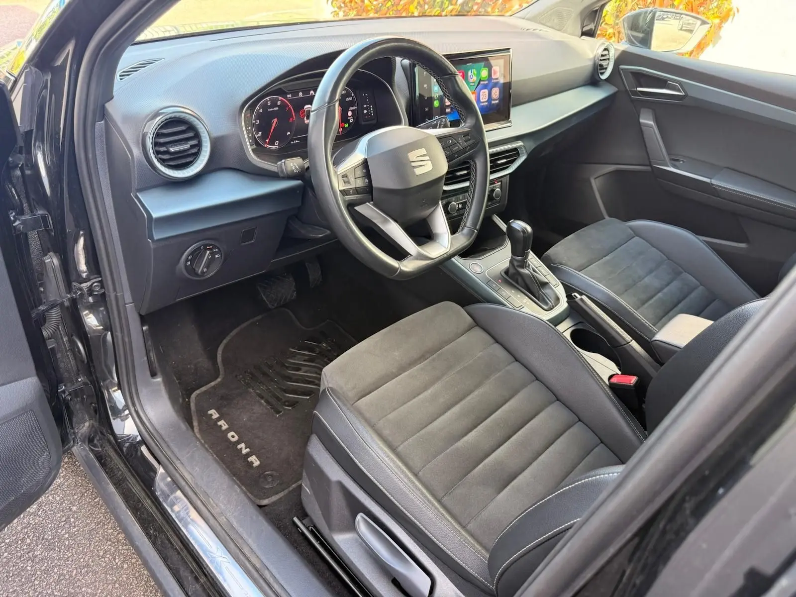 Vue intérieure côté conducteur du SEAT Arona 2022, avec sièges noirs, volant cuir multifonctions et écran tactile central.