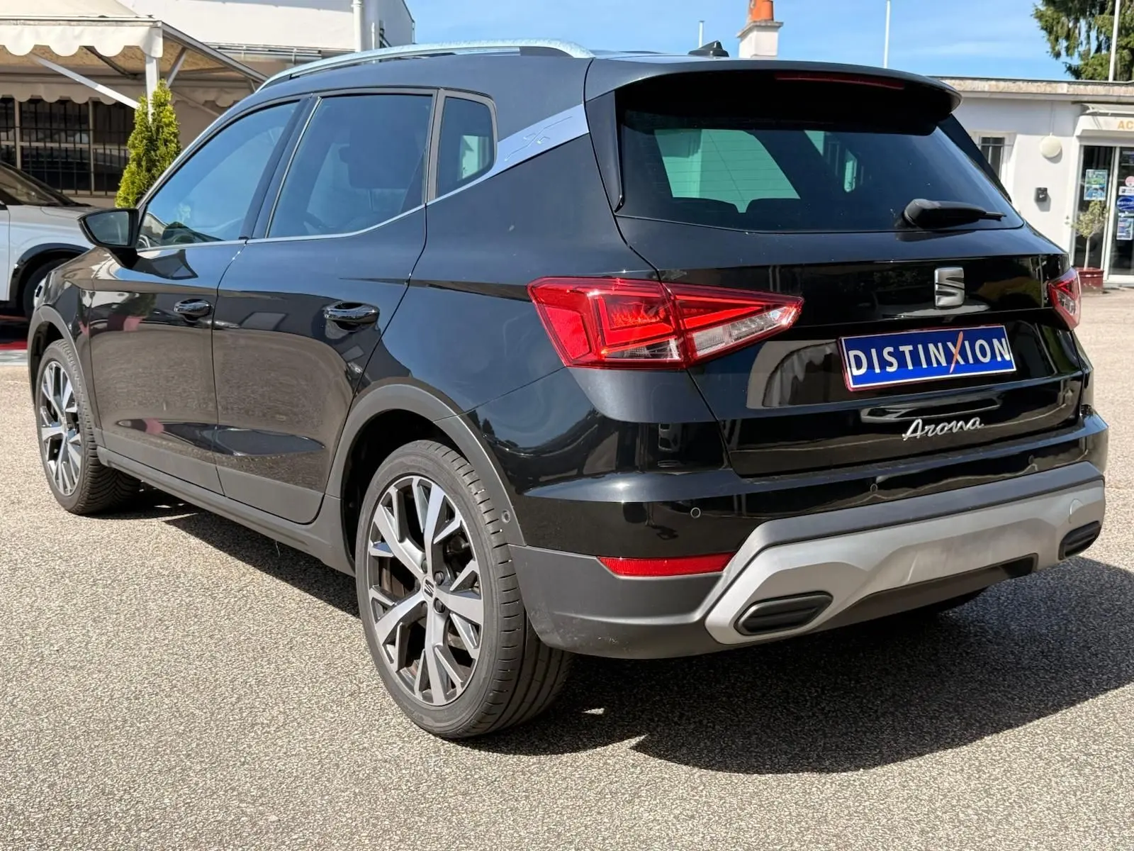 Vue 3/4 arrière droite d'une SEAT Arona noire avec jantes alliage et toit noir mat, stationnée en extérieur.