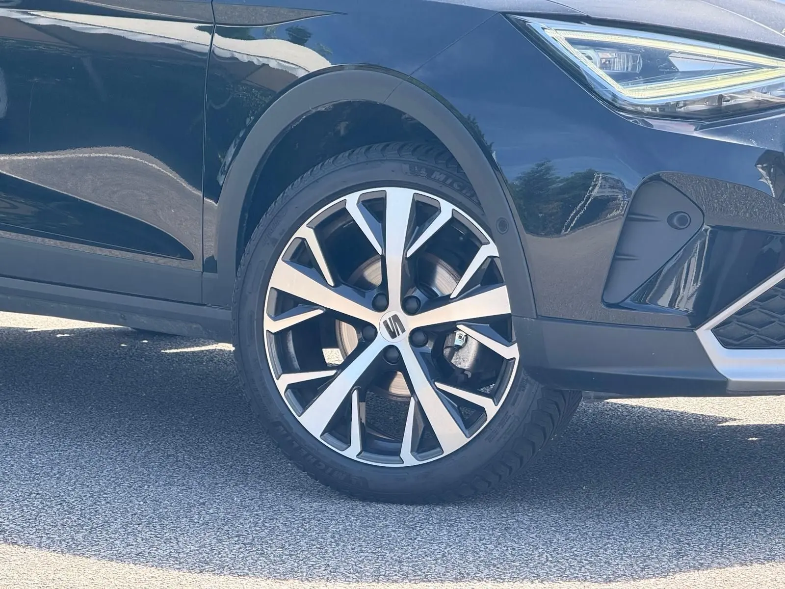Gros plan sur la roue avant droite et partie avant d’un SEAT Arona 2022 couleur sombre avec jante alu bicolore.