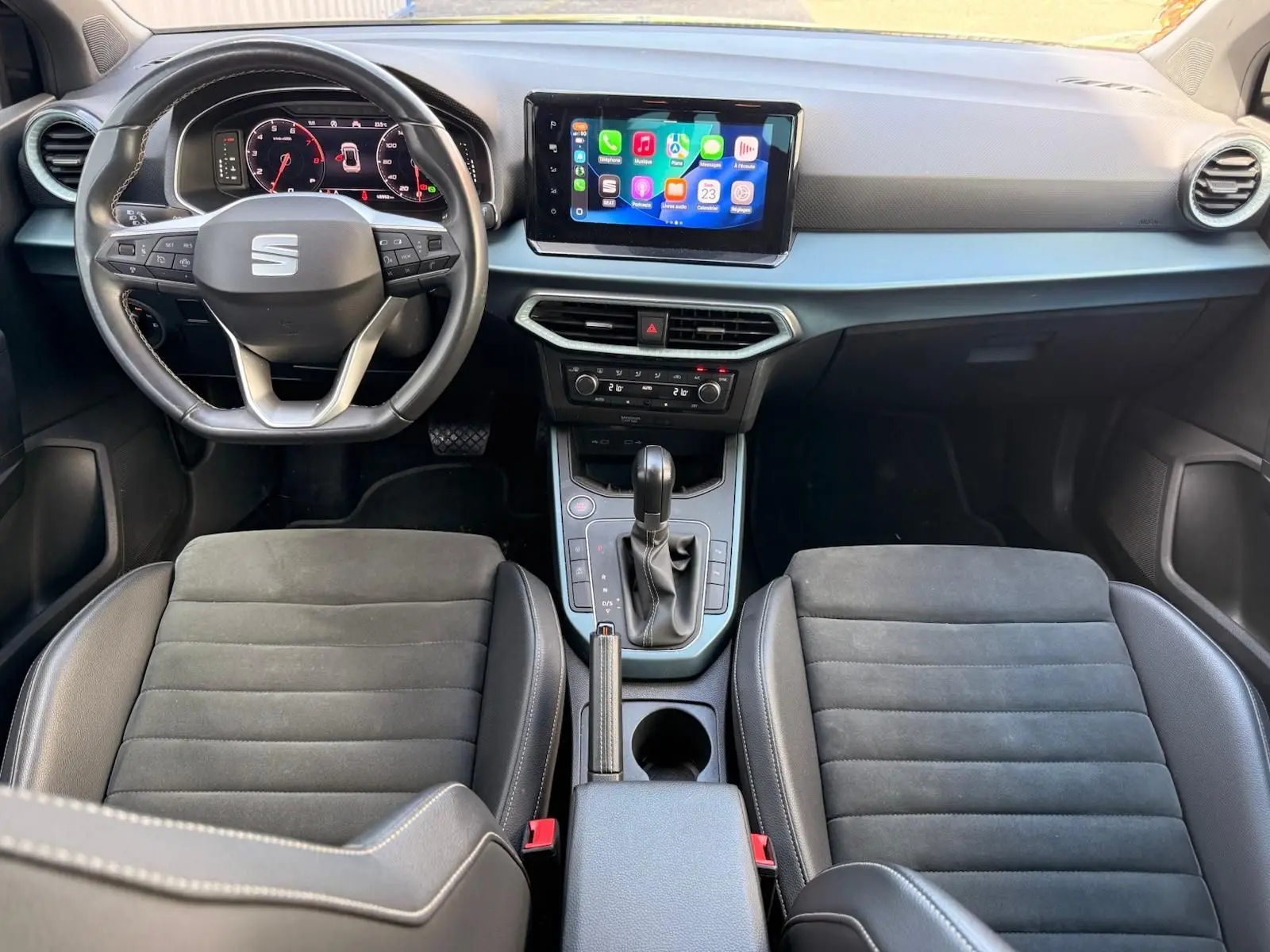 Vue intérieure avant du SEAT Arona 2022 avec tableau de bord moderne, écran tactile central et sièges noirs en tissu et cuir.