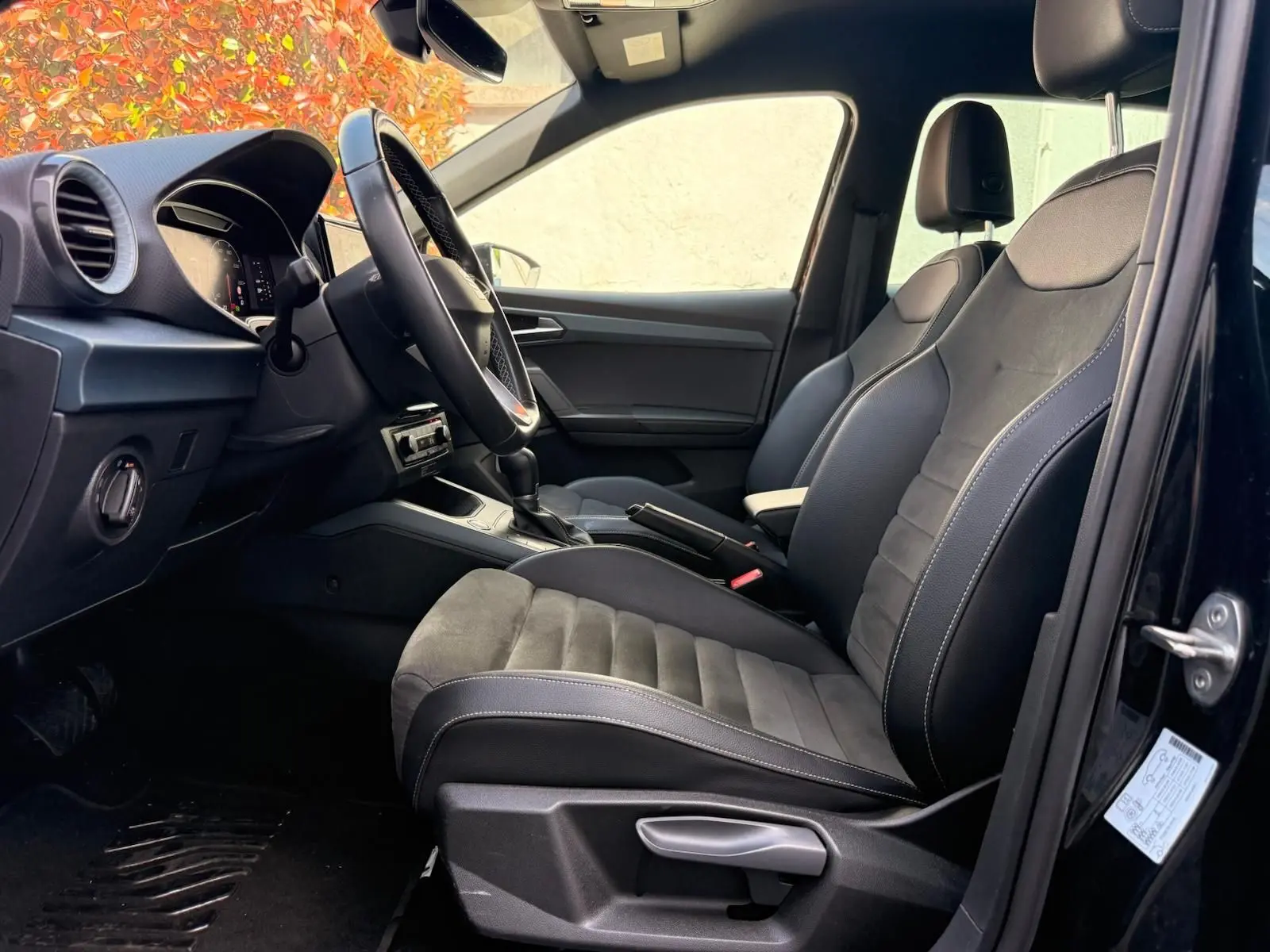 Vue intérieure côté conducteur de la SEAT Arona 2022, sièges noirs avec surpiqûres blanches et volant cuir alu.