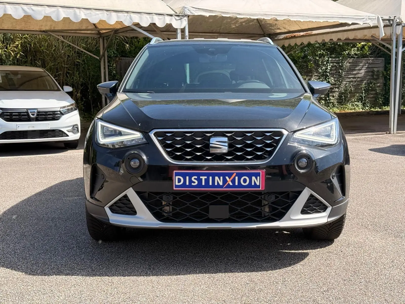 Vue avant d'un SEAT Arona noir avec calandre chromée et plaques Distinxion sous un auvent.