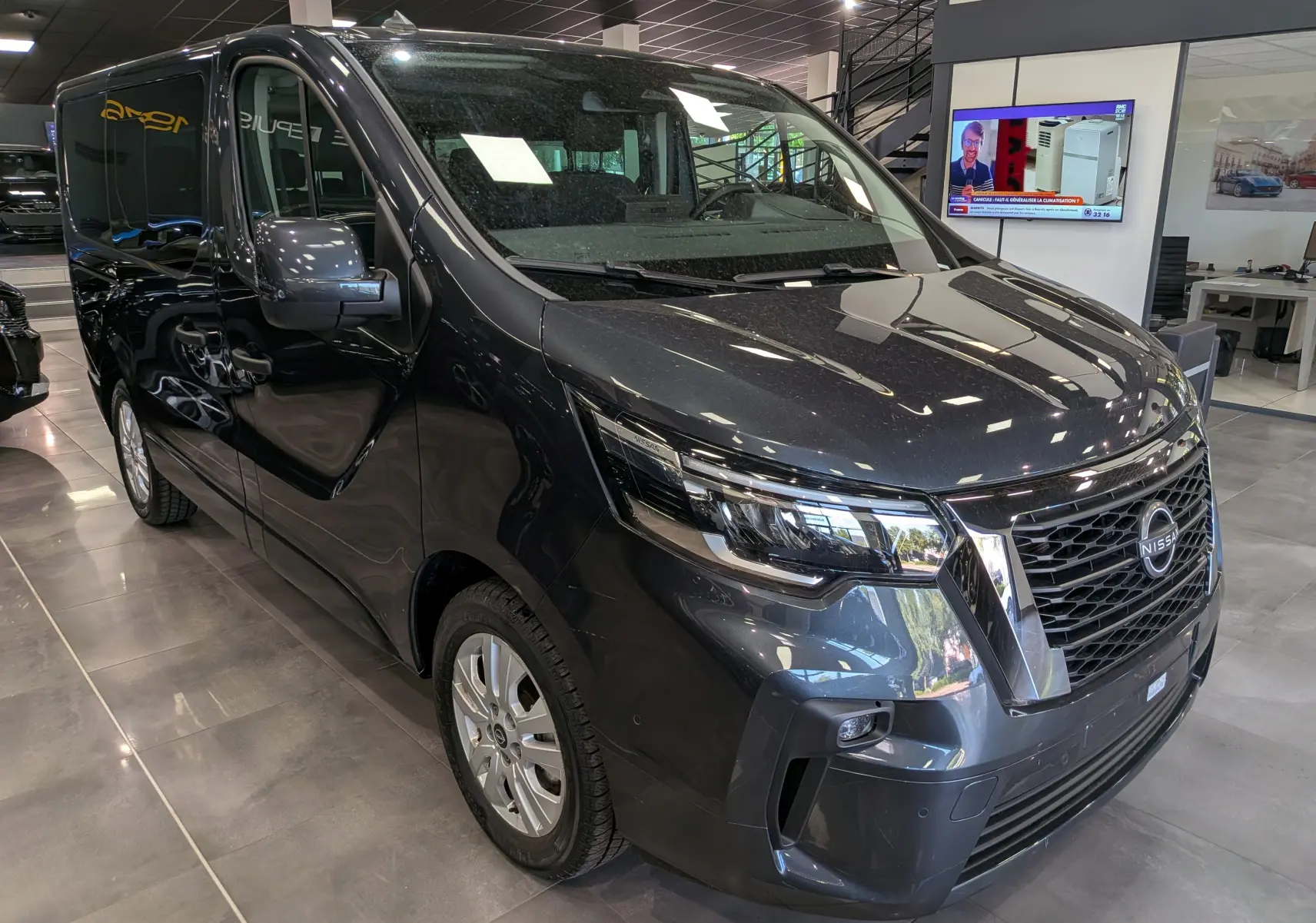 Vue 3/4 avant droit du Nissan Primastar Combi gris comète, mettant en valeur sa calandre chromée et ses phares modernes.