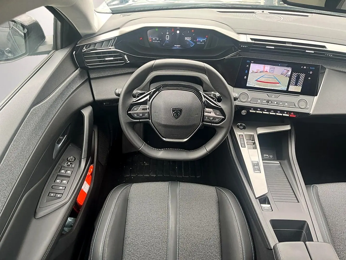 Vue intérieure avant centrée sur le volant noir multifonction et l’écran tactile affichant la caméra de recul de la Peugeot 308.
