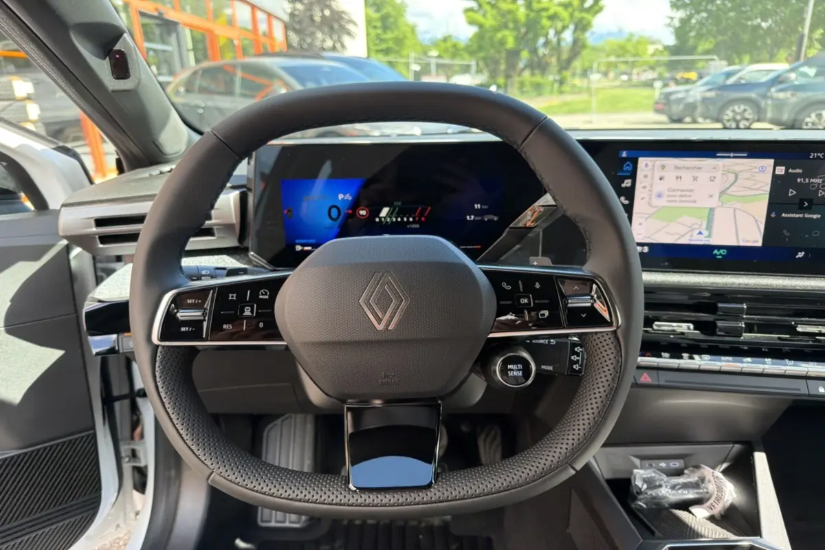 Vue intérieure centrée sur le volant multifonctions de la Renault Clio blanc glacier avec tableau de bord numérique et écran tactile.