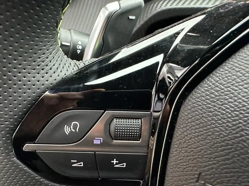 Gros plan sur les commandes noires du volant perforé de la Peugeot 208 1.2 Hybrid 110ch GT 2025.