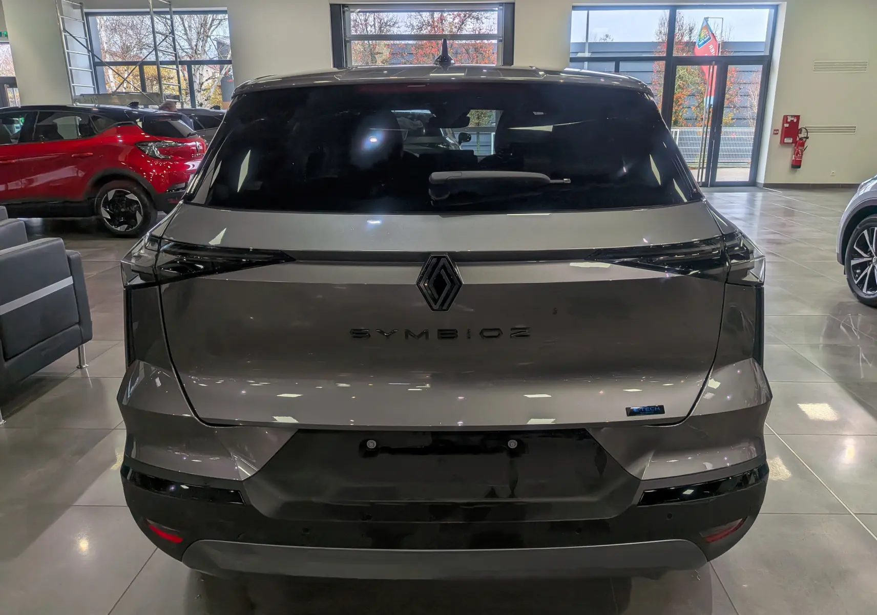 Vue arrière d'un Renault SYMBIOZ gris Cassiopé en showroom, avec logo et badge E-Tech visible sur le hayon.