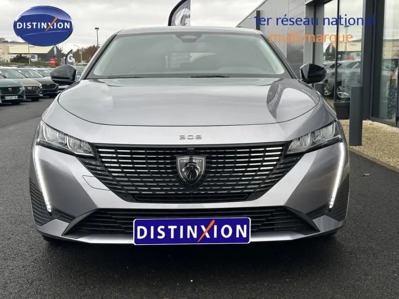 Vue frontale d'une Peugeot 308 1.2 PureTech gris Artense avec calandre noire et feux LED verticaux allumés.