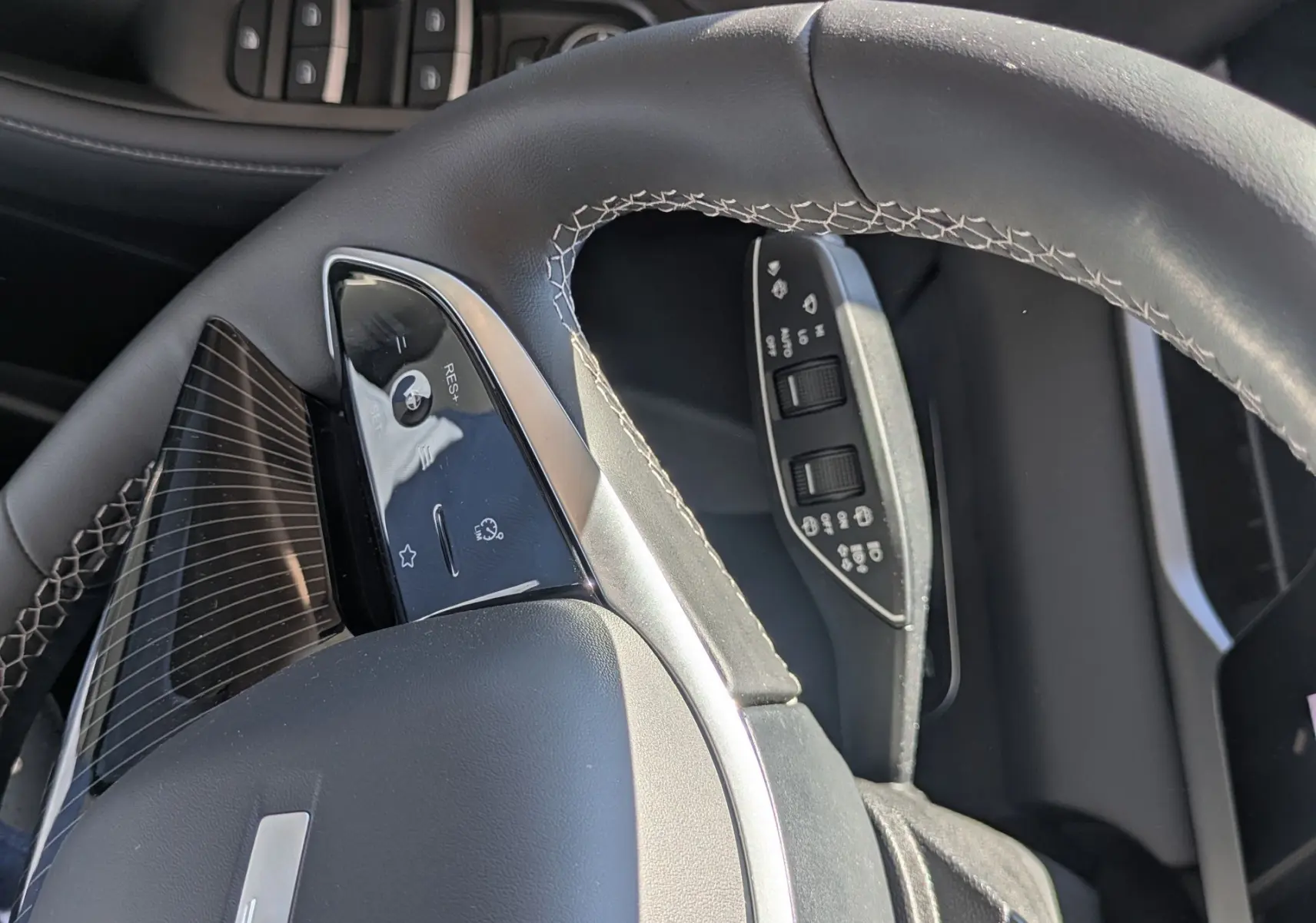 Vue rapprochée du volant cuir noir avec surpiqûres blanches et commandes intégrées du JAECOO J5, côté conducteur.