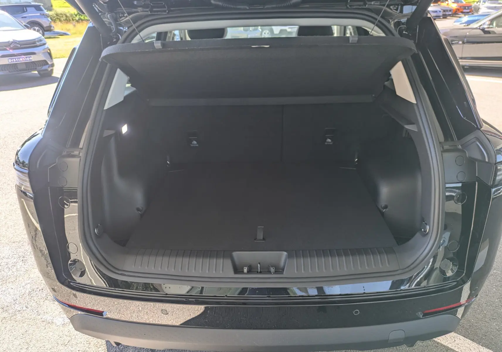 Coffre ouvert vu de l'arrière d'un JAECOO J5 noir carbone métal, montrant un espace de chargement spacieux et propre.