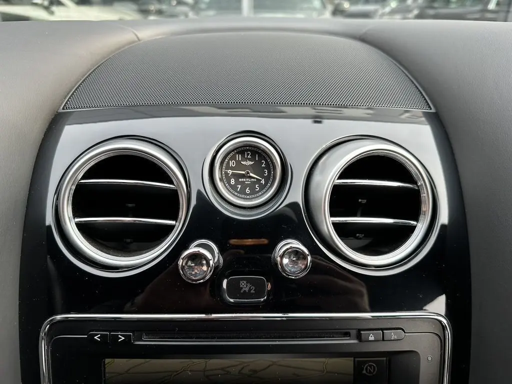 Gros plan sur l'horloge Breitling et les aérateurs ronds chromés du tableau de bord noir d'une Bentley Continental GT Mulliner 2013.