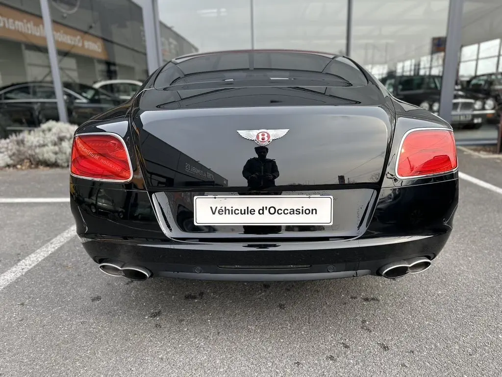 Vue arrière d'une Bentley Continental GT 4.0 V8 Mulliner noire de 2013 avec feux rouges et double sortie d'échappement chromée.