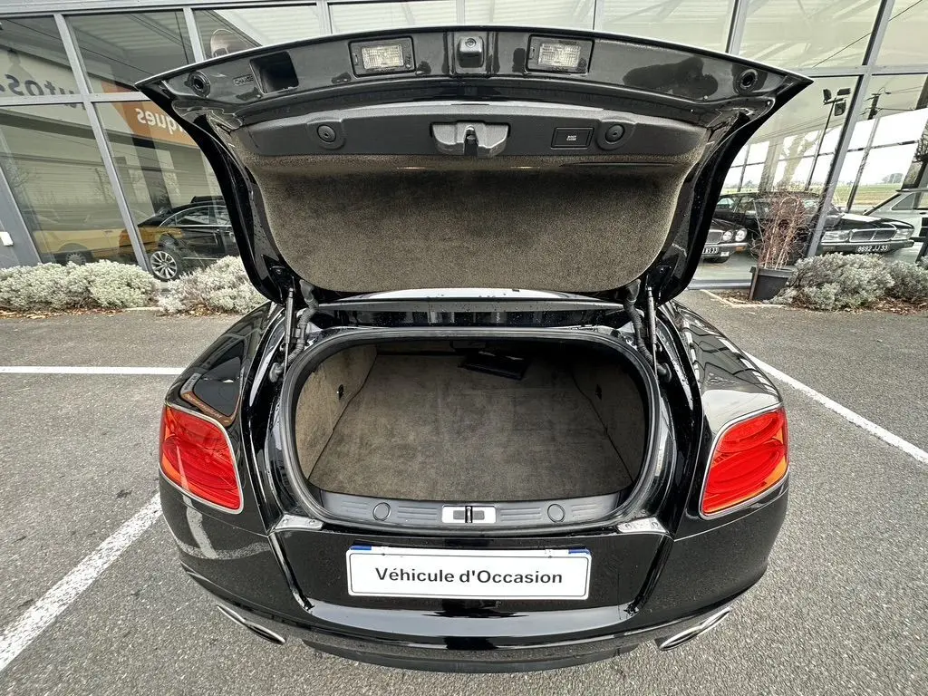 Vue arrière d'une Bentley Continental GT Mulliner noire de 2013 avec coffre ouvert et intérieur de coffre beige visible.