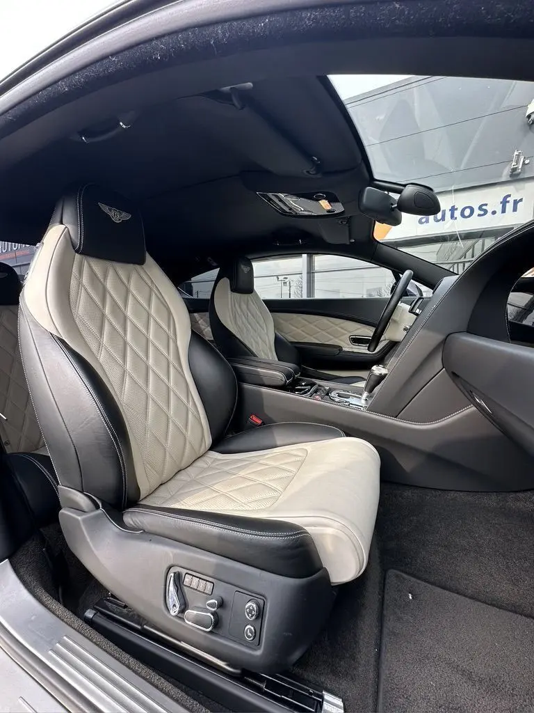 Intérieur de Bentley Continental GT 2013, vue côté gauche sur sièges cuir noir et beige matelassé avec logo Mulliner brodé.