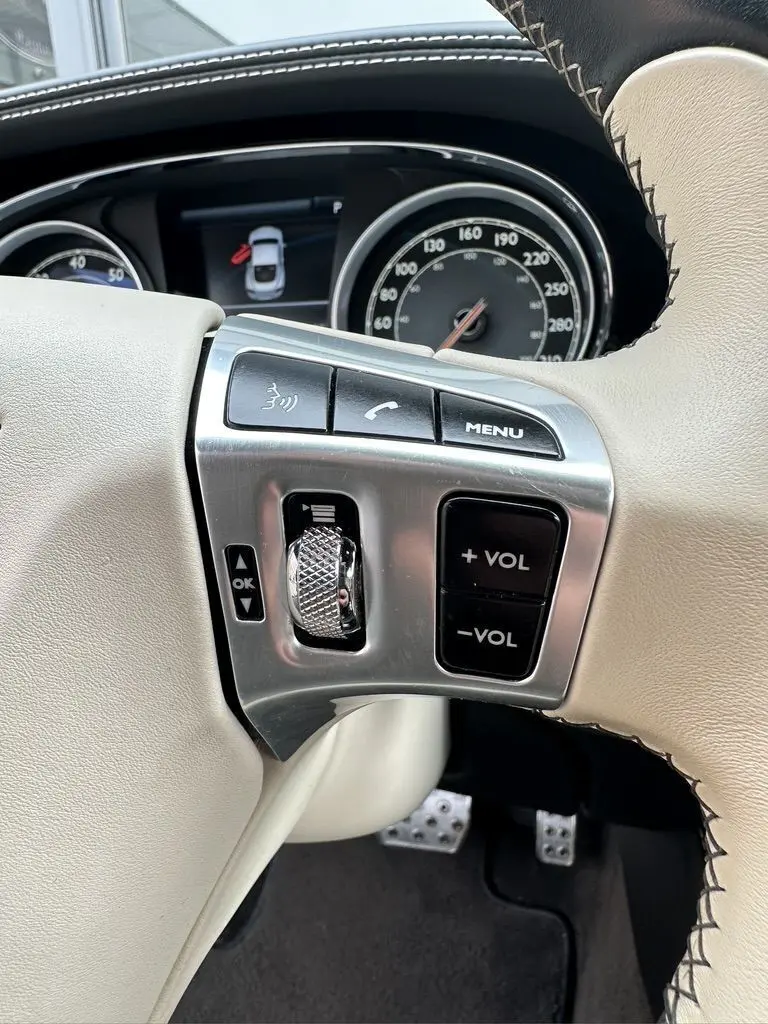 Gros plan sur le volant beige de la Bentley Continental GT Mulliner 2013, avec commandes audio et tableau de bord visible.