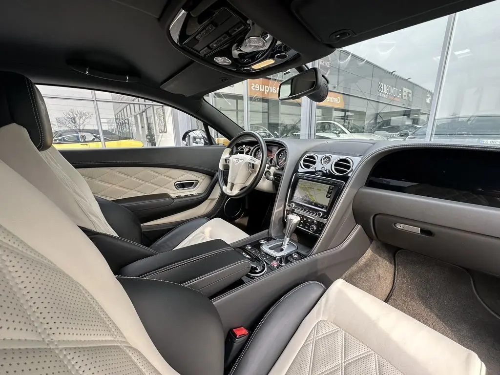 Vue intérieure côté conducteur de la Bentley Continental GT Mulliner 2013 noire avec sellerie cuir beige et noire raffinée.