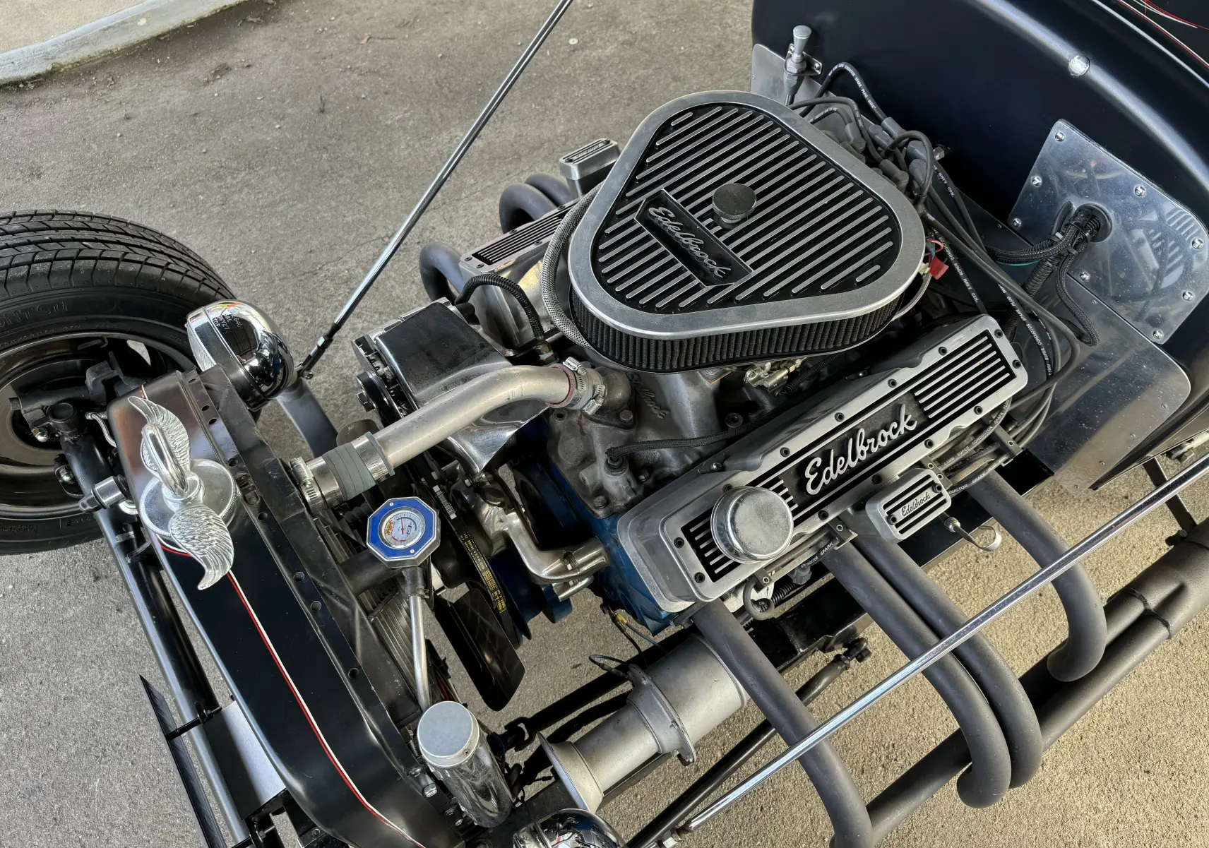 Gros plan sur le moteur V8 Edelbrock d'un Ford T Hot Rod noir, avec détails chromés et liserés rouges faits main.