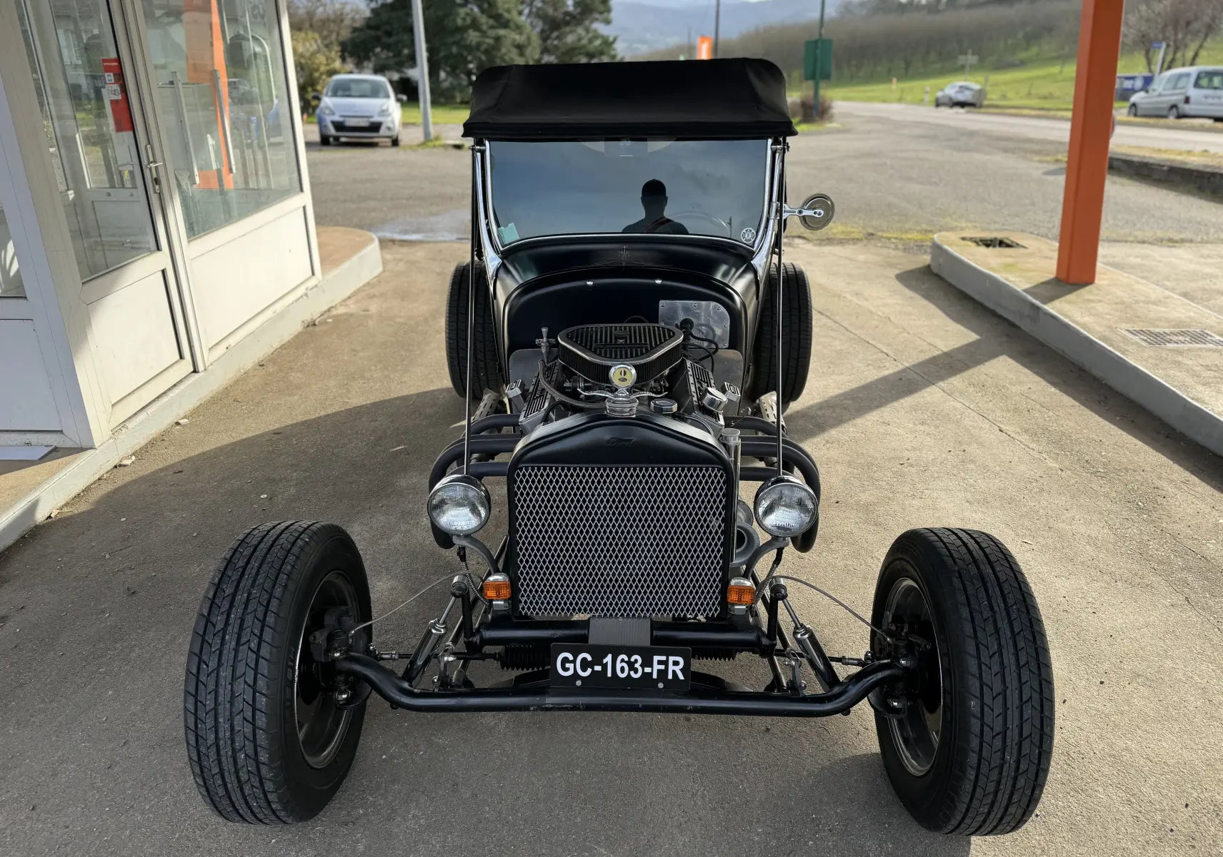 Vue frontale d'une Ford T Hot Rod V8 noire de 1923, moteur visible et capote noire relevée.