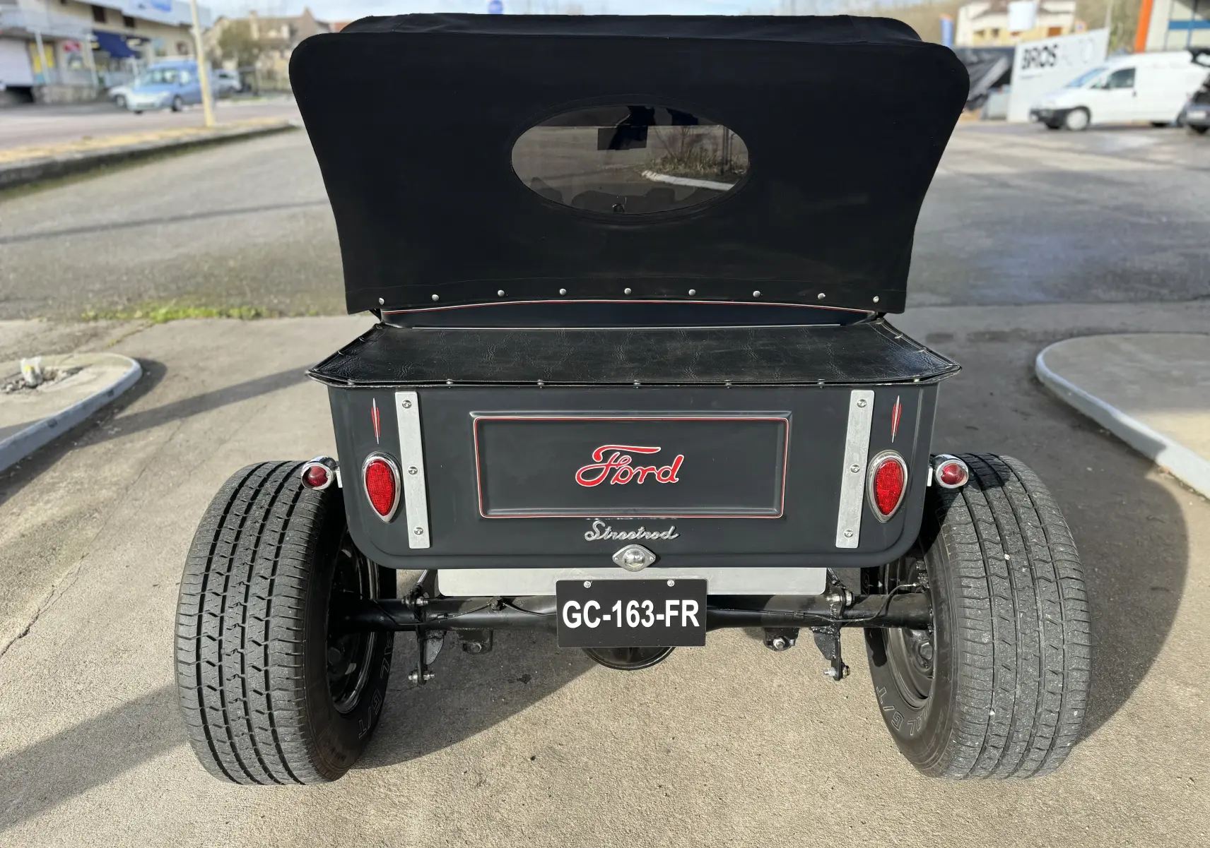 Vue arrière d'une Ford T Hot Rod V8 noire avec capote relevée et feux ronds rouges distinctifs.