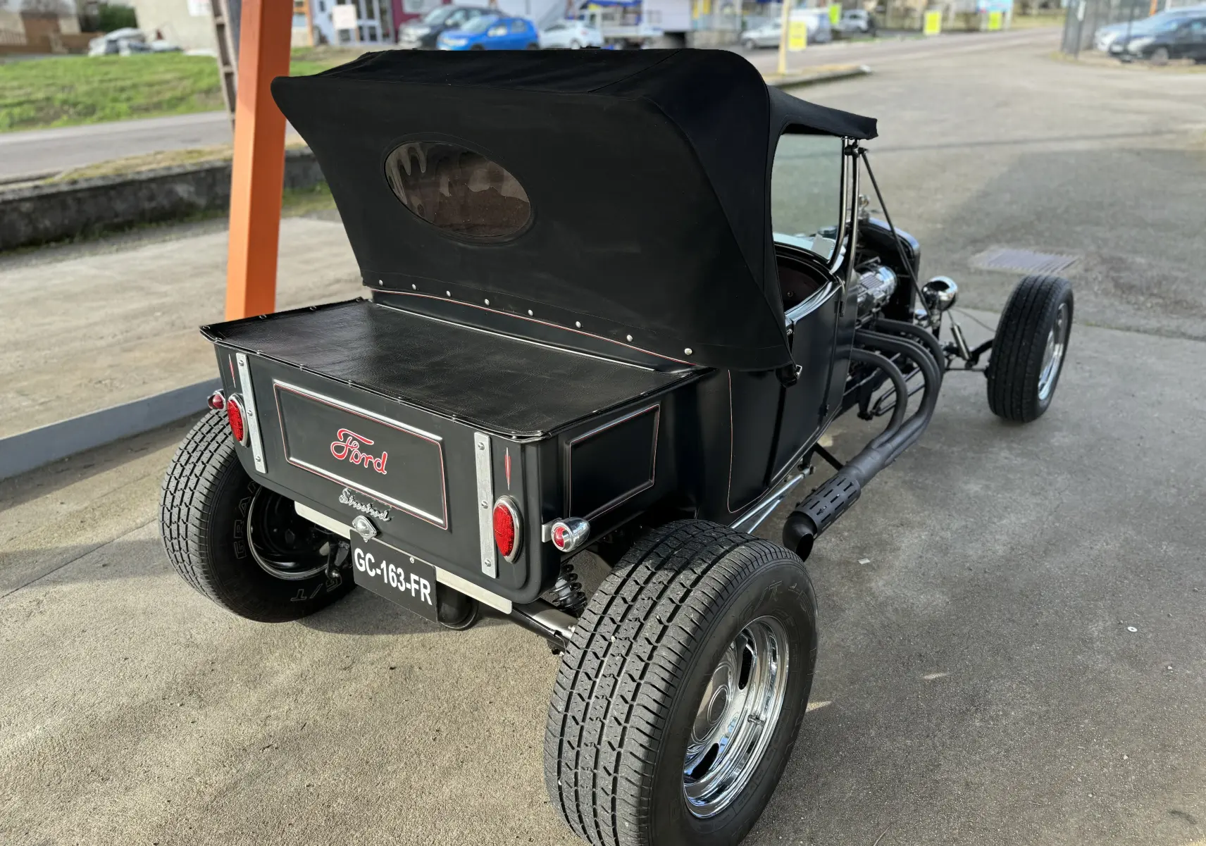 Vue 3/4 arrière droite d'une Ford T Hot Rod V8 noire décapotable avec coffre et pneus larges chromés.