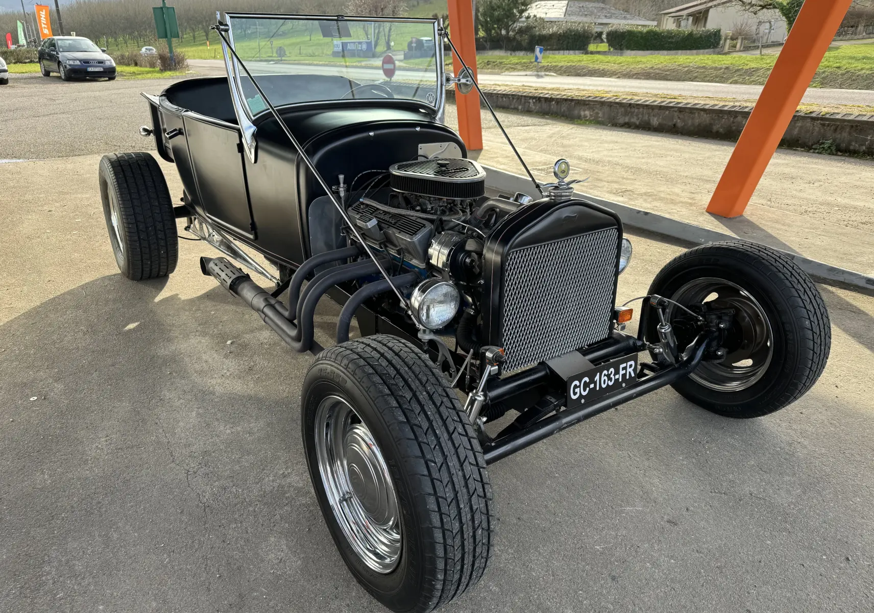 Ford T Hot Rod V8 noir vu en 3/4 avant droit, moteur apparent et carrosserie décapotable mate.