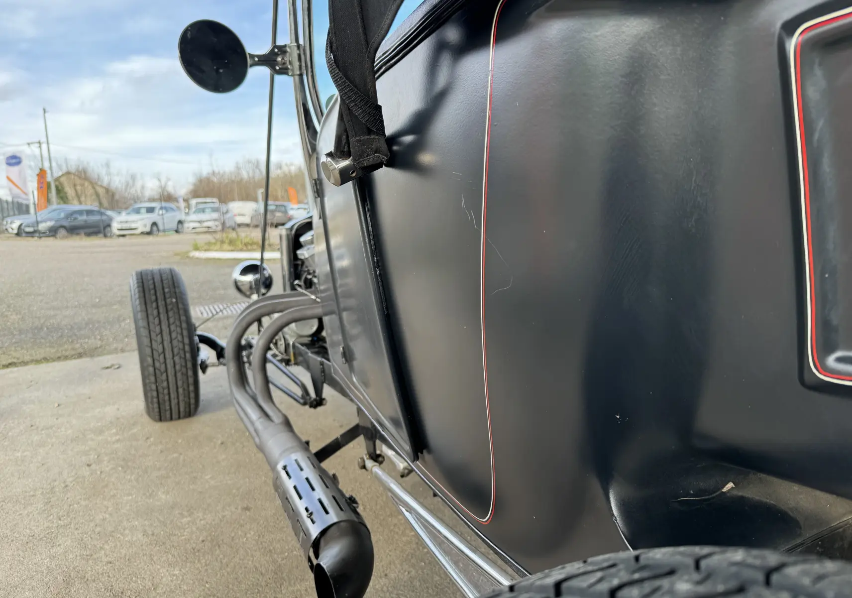 Vue latérale gauche rapprochée du Ford T Hot Rod noir mat avec liserés rouges et échappement latéral chromé.