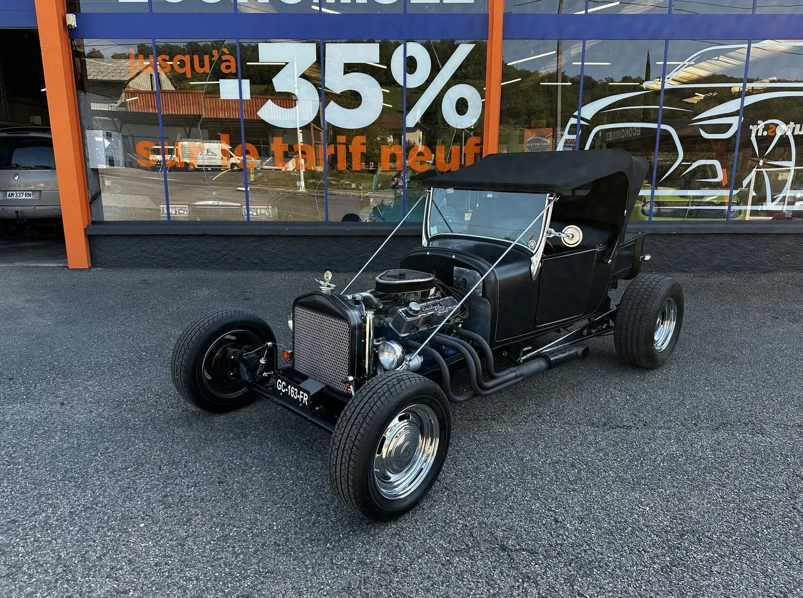 Ford T Hot Rod V8 noir vue 3/4 avant droit, capote noire et moteur V8 apparent avec échappements latéraux.